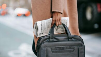 crop businesswoman with newspaper crossing road